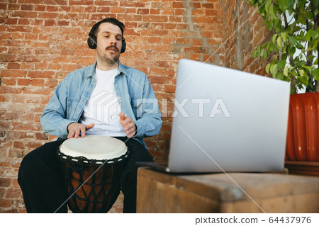 Caucasian musician playing hand drum during online concert at home isolated and quarantined, improvising Caucasian musician playing hand drum during online concert at home isolated and quarantined, improvising 64437976