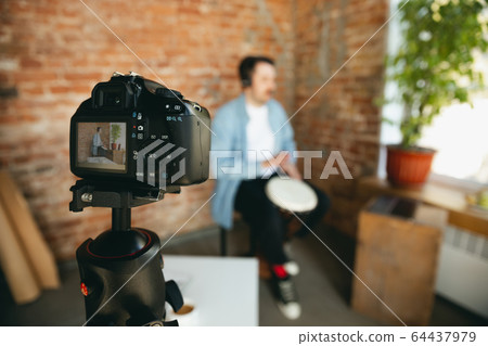 Caucasian musician playing hand drum during online concert at home isolated and quarantined, focus on camera 64437979