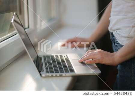 Close up of Female in mask working at home. Woman put laptop on windowsill and work Close up of Female in mask working at home. Woman put laptop on windowsill and work 64438488
