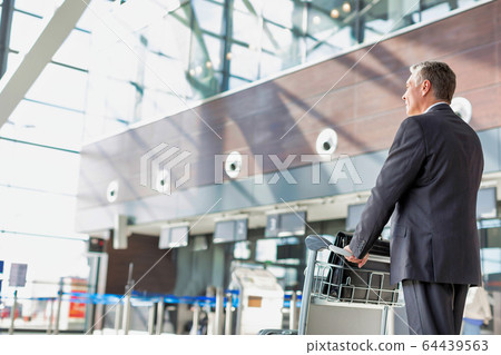 Mature businessman pushing baggage cart for check Mature businessman pushing baggage cart for check 64439563