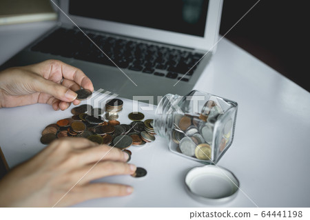 Woman's hand saving and counting money coins in the glass jar with computer laptop 64441198