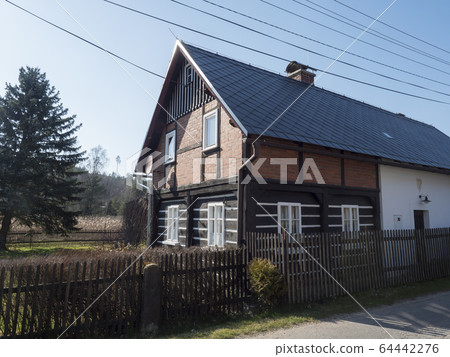 View from road on old rustic cottage half timbered house in small village Marenicky in luzicke hory, Lusatian Mountains, arly spring, blue sky 64442276