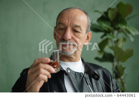 Senior man with beard and mustache holds glass of brandy or whisky. Alchol degustation, tasting concept Senior man with beard and mustache holds glass of brandy or whisky. Alchol degustation, tasting concept 64443061