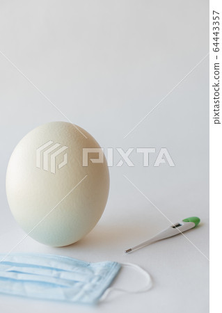 Large white easter ostrich egg, medical mask and thermometer. Egg, respirator and thermometer. Easter and Coronavirus, Covid-19. Ostrich egg, medical mask and thermometer on a white background. 64443357