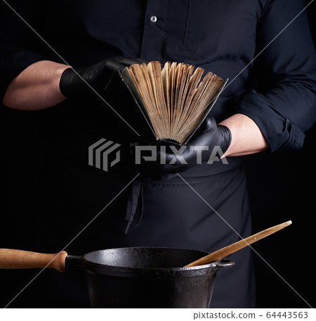 male cook in a black uniform holds an old cookbook 64443563