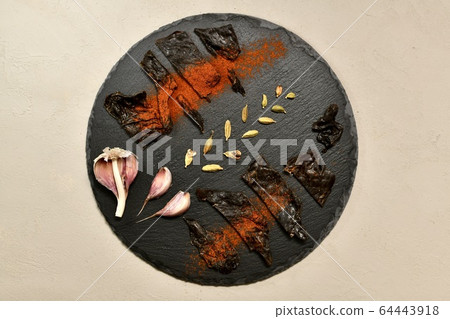 The horse meat is spread on a round black with red pepper cardamom with a peeled garlic in the center on stucco. The horse meat is spread on a round black with red pepper cardamom with a peeled garlic in the center on stucco. 64443918