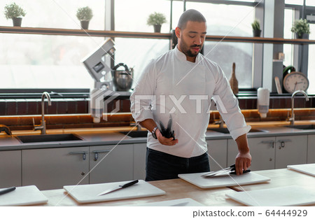 Handsome young chef African ethnicity lays knives on table in front of a culinary master class. Handsome young chef African ethnicity lays knives on table in front of a culinary master class. 64444929