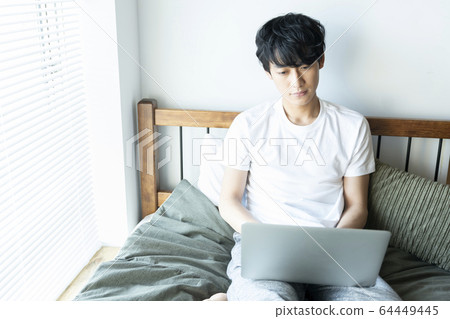 A young man sitting in bed and operating a computer Male in his 20s Lifestyle 64449445