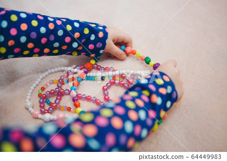 a child plays with colored beads. a girl becomes a little lady. Concept of fine motor skills development, educational games, childhood, children's day, kindergarten. Ads for costume jewelry and fashio a child plays with colored beads. a girl becomes a little lady. Concept of fine motor skills development, educational games, childhood, children's day, kindergarten. Ads for costume jewelry and fashio 64449983