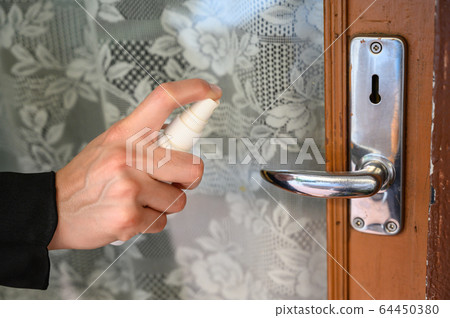 Shot of someone hand using alcohol hand sanitizer spraying on the door knob before open it. Hand sanitizer used to decrease infectious or kills germs, bacteria even more coronavirus. 64450380