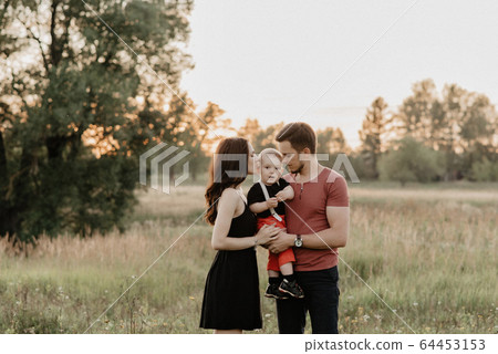 young mom and dad hug their son in summer in a field at sunset 64453153