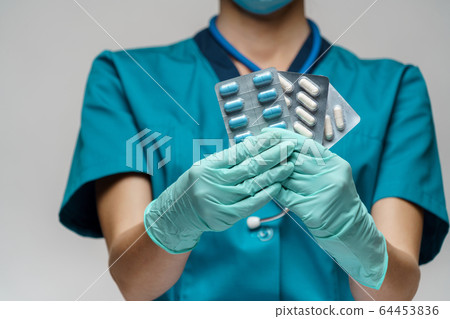 medical doctor nurse woman wearing protective mask and rubber or latex gloves - holding blisters of pills medical doctor nurse woman wearing protective mask and rubber or latex gloves - holding blisters of pills 64453836