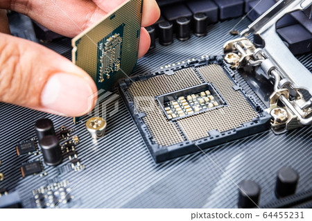Closeup detail of CPU Chip over socket with hand of a modern computer black motherboard. Electronic small component details. Select focus 64455231