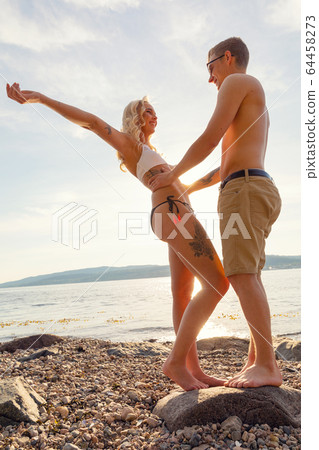 Happy and Smiling Young Couple Standing On Rock At Beach 64458273