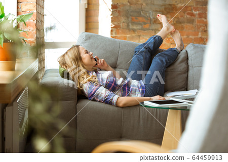 Young woman studying at home during online courses or free information by herself, talking on phone, lying on sofa, laughting Young woman studying at home during online courses or free information by herself, talking on phone, lying on sofa, laughting 64459913