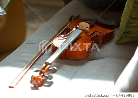 Close up shoot of violin lying on sofa in sunlight, hobby and music concept Close up shoot of violin lying on sofa in sunlight, hobby and music concept 64459998