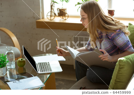 Young woman studying at home during online courses or free information by herself, making notes Young woman studying at home during online courses or free information by herself, making notes 64459999