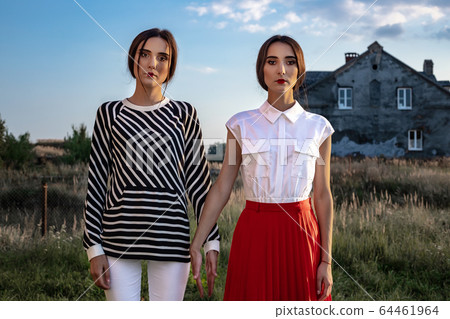 Outdoor fashion portrait of two young beautiful women wearing fashionable clothes posing on the street 64461964
