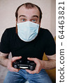 Adult balding white man playing video games with medical mask on his face while Covid-19 quarantine 64463821