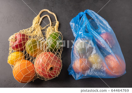 Bunch of mixed organic fruit, vegetables and greens in a string bag and plastic on dark background 64464769