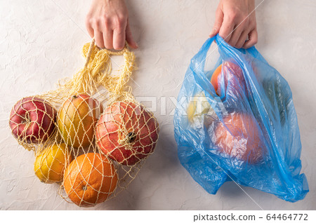 Woman hands hold mixed organic fruit, vegetables and greens in a string bag and plastic on light 64464772