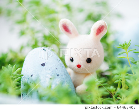 Cute Easter rabbit with light blue egg. Easter celebration concept. White toy bunny in green grass. Cute Easter rabbit with light blue egg. Easter celebration concept. White toy bunny in green grass. 64465405