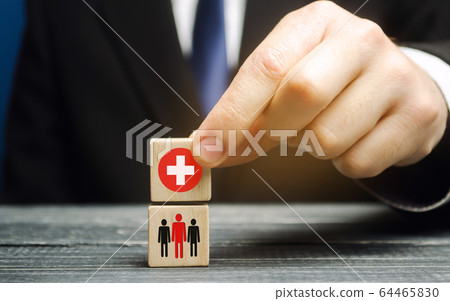 A man holds a block with a medical cross and people. Healthcare, medicine and charity concept. Health insurance. Ambulance. Coronavirus pandemic infection COVID-19. A man holds a block with a medical cross and people. Healthcare, medicine and charity concept. Health insurance. Ambulance. Coronavirus pandemic infection COVID-19. 64465830