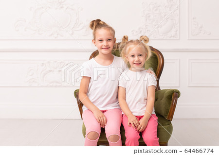 Two little blond sit in green armchair and hug each other 64466774