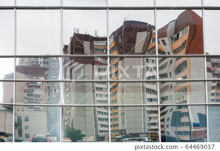 Distorted reflection of multi-storied residential buildings in mirrors of shopping center opposite. Distorted reflection of multi-storied residential buildings in mirrors of shopping center opposite. 64469037