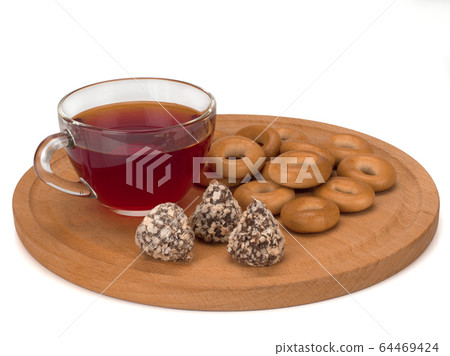 Fresh dry bagels, three candies on a wooden board and a cup of tea isolated on white background Fresh dry bagels, three candies on a wooden board and a cup of tea isolated on white background 64469424