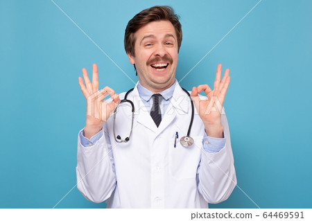 Smiling male doctor in white coat showing ok hand Smiling male doctor in white coat showing ok hand 64469591