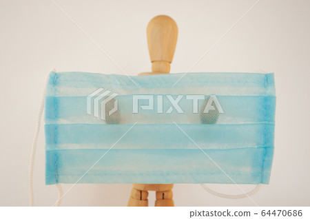 A wooden man holds a blue medical protective mask with space for text. A concept of protection during a coronavirus pandemic. Copy space. A wooden man holds a blue medical protective mask with space for text. A concept of protection during a coronavirus pandemic. Copy space. 64470686