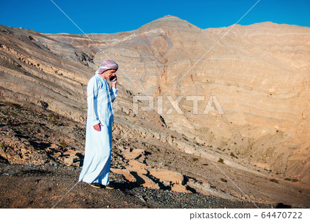 Arab man using phone with sandstone mountain Arab man using phone with sandstone mountain 64470722