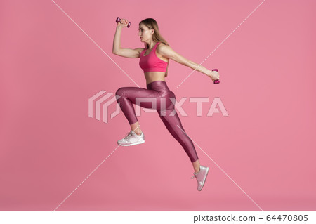 Beautiful young female athlete practicing on pink studio background, monochrome portrait 64470805