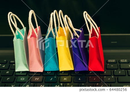 Row colorful paper shopping bags with mobile phone on a laptop keyboard. Ideas about online shopping or shopping at home or office which customers can purchase items or services or goods remotely. Row colorful paper shopping bags with mobile phone on a laptop keyboard. Ideas about online shopping or shopping at home or office which customers can purchase items or services or goods remotely. 64480256