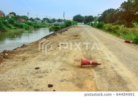 The old traffic cone falling on the road that was being repaired along the irrigation canal for agriculture. The old traffic cone falling on the road that was being repaired along the irrigation canal for agriculture. 64484991