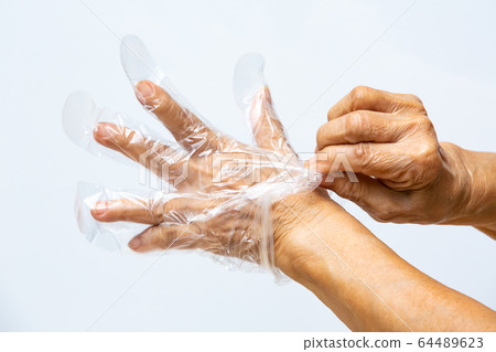Senior woman's hands wearing disposable protective plastic glove on grey background, Close up shot, Prevention from covid19, Coronavirus, Bacteria, Healthcare 64489623