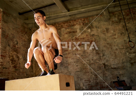 Jumping athlete on wooden box in gym 64491221