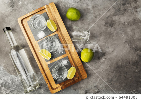 Tequila bottle and shots, limes, salt on wooden Tequila bottle and shots, limes, salt on wooden 64491303