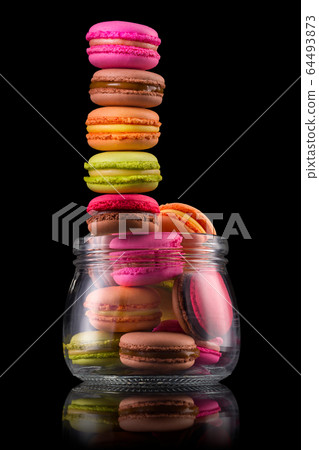Flying french colorful macaroons and jar on wooden table isolated on black Flying french colorful macaroons and jar on wooden table isolated on black 64493873