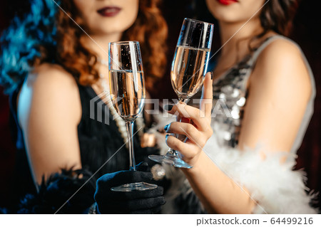 Close up glasses of champagne. Flappers women wearing in style of Roaring Gatsby twenties drinking 64499216