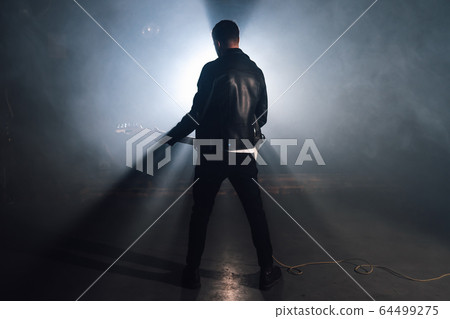 Rock guitarist man in leather jacket in smoky studio or stage masterfully playing electric guitar Rock guitarist man in leather jacket in smoky studio or stage masterfully playing electric guitar 64499275