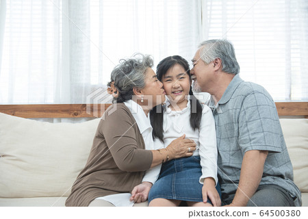 Asian grandparents kiss granddaughter cheek at home 64500380