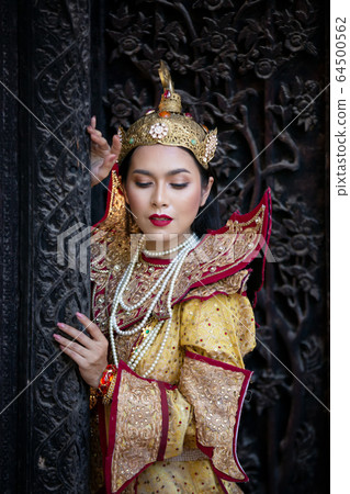 Portrait of an Asian Women in Mandalay, Myanmar Woman with golden Traditional Clothes are Standing Against Art Carving Wooden Door. 64500562