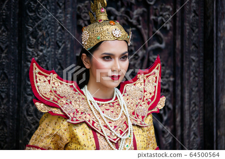 Portrait of an Asian Women in Mandalay, Myanmar Woman with golden Traditional Clothes are Standing Against Art Carving Wooden Door. 64500564