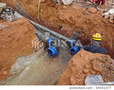Underground utility and services pipe laid by workers in the trenches at the construction site. Installation of stop cork valve and joint in progress.    64501077