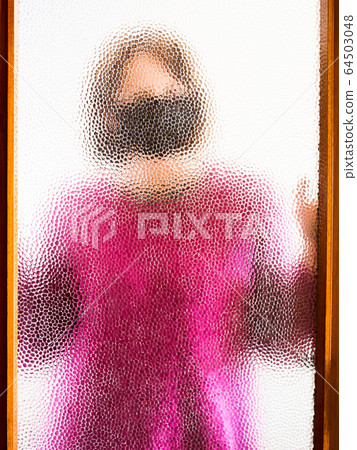 Woman in face mask behind door glass against covid 64503048