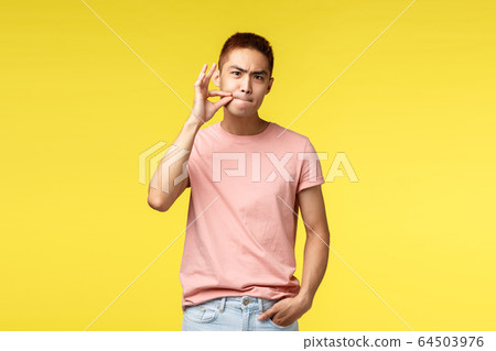 You better shut your mouth. Portrait of annoyed and serious young asian man show zip on lips, seal them as prohibit not tell anyone secret, demand silence, standing bothered yellow background 64503976