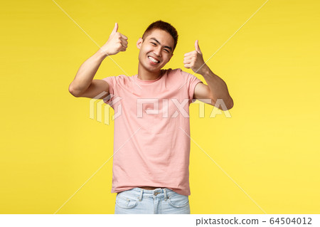Lifestyle, travel and people concept. Happy asian man in pink t-shirt satisfied with awesome product, show thumbs-up and smiling broadly, guarantee you like it, approve promo, yellow background Lifestyle, travel and people concept. Happy asian man in pink t-shirt satisfied with awesome product, show thumbs-up and smiling broadly, guarantee you like it, approve promo, yellow background 64504012