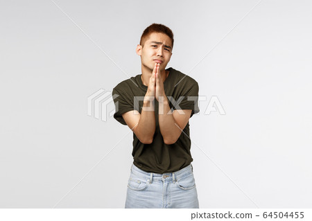 Clingy taiwanese teenage guy begging parents let him go party, shaking pleading hands, clasp arms together in pray and frowning, asking help, appologizing, standing grey background 64504455